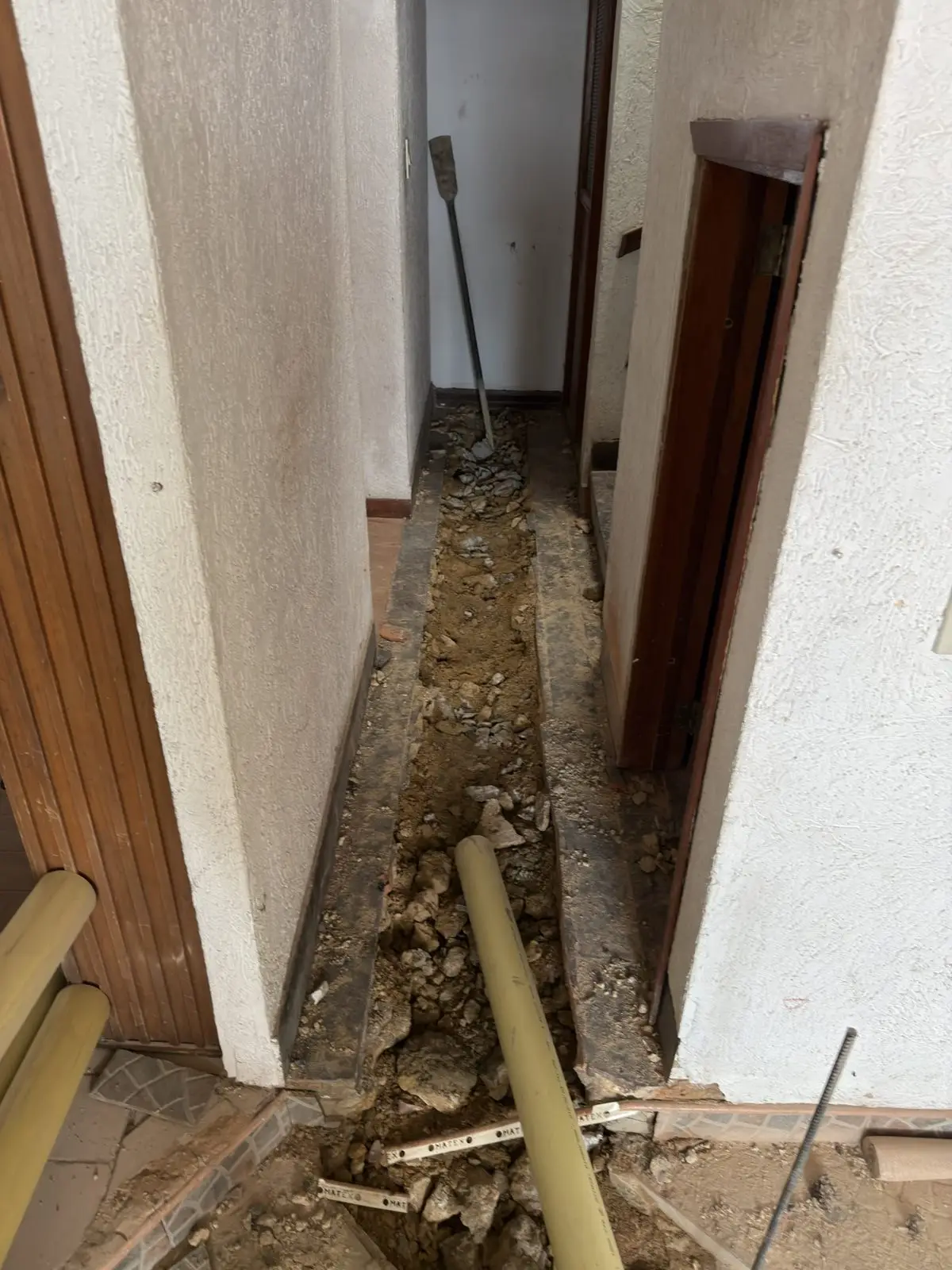 Zanja con tubería PVC nueva a lo largo de un pasillo de vivienda